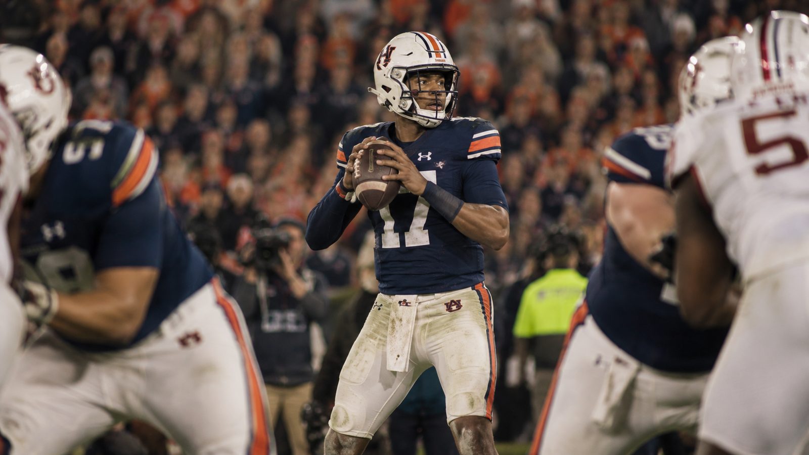A quarterback at the top of his drop under stadium lights